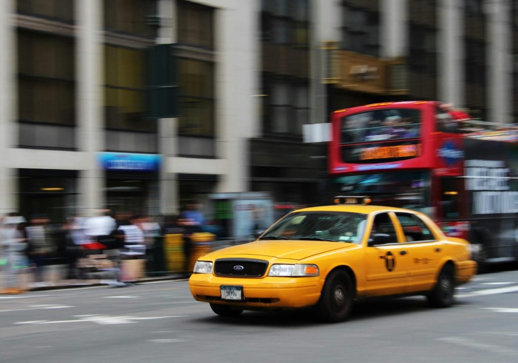 A yellow taxi speeds through the vibrant streets of New York City, capturing urban life and motion.