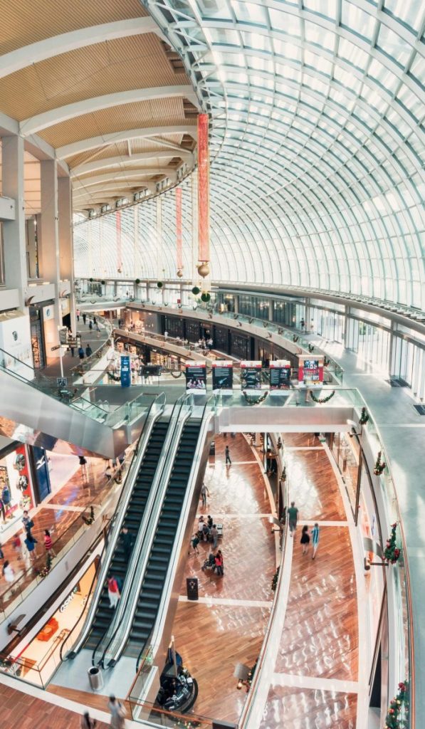Spacious indoor shopping mall with glass ceilings and a modern design, including escalators and shops.